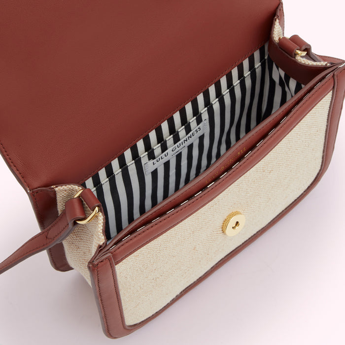 Inside of a Lulu Guinness crossbody bag, featuring a cream canvas exterior and brown leather trim. The interior lining is black and white striped.