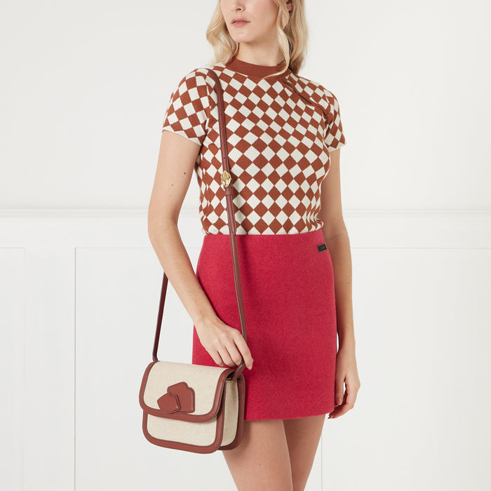 Woman in a brown and white checkered top and a red mini skirt wearing a brown and beige crossbody bag.