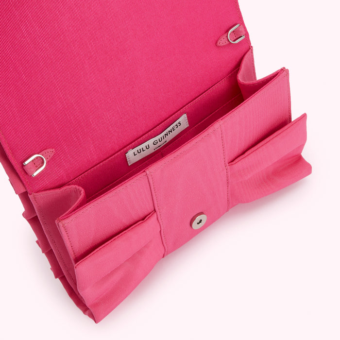 Pink Lulu Guinness bow clutch open to reveal interior and brand label.