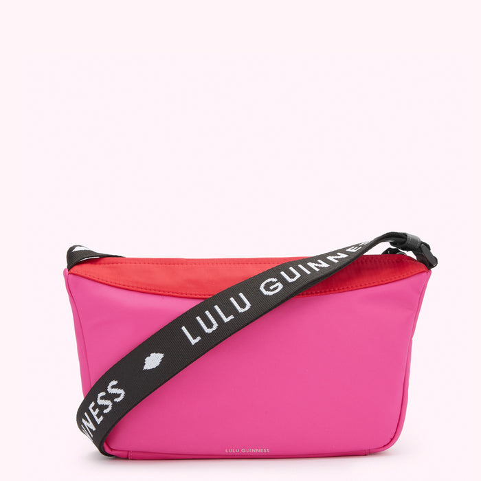 A front image of a hot pink nylon crossbody bag with contrasting red top panel and black 'Lulu Guinness' branded strap.