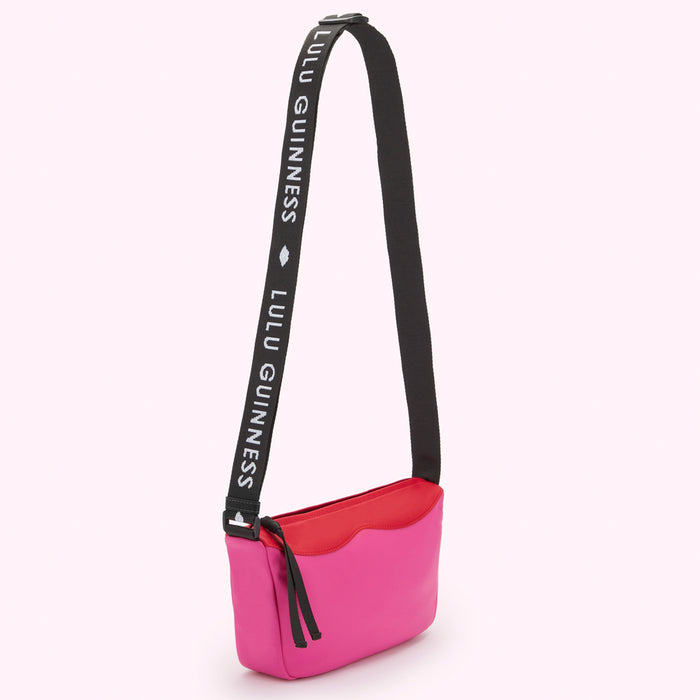 Bright pink, red and black Lulu Guinness nylon crossbody bag with a black shoulder strap that says "Lulu Guinness."