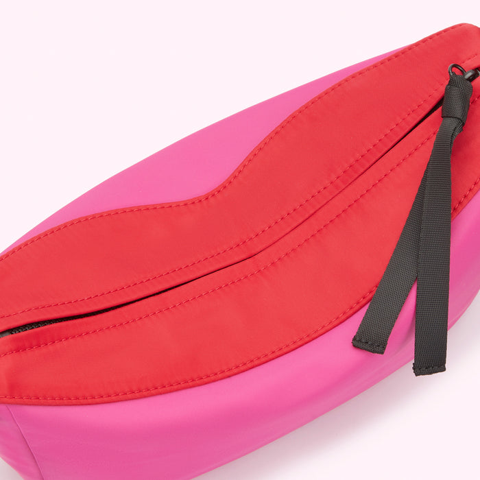 Close-up of a bright pink and red nylon crossbody bag zip with black ribbon zip pull.