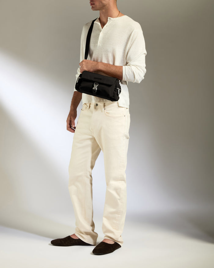 a man in white pants and white sweater holding a black bag