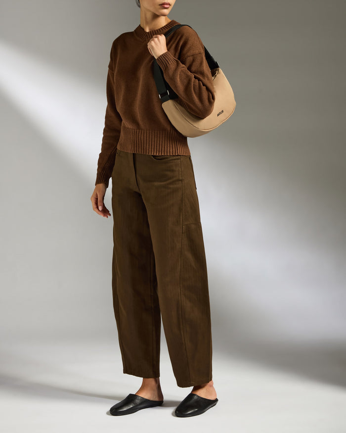 a woman in brown pants and a sweater holding a purse