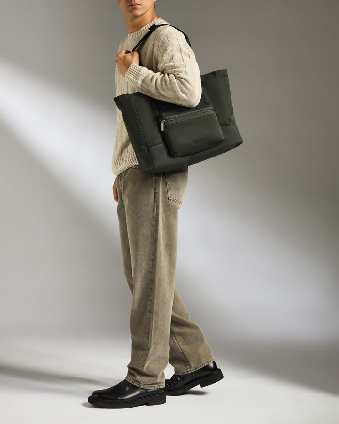 a man in a white sweater and brown pants holding a black bag