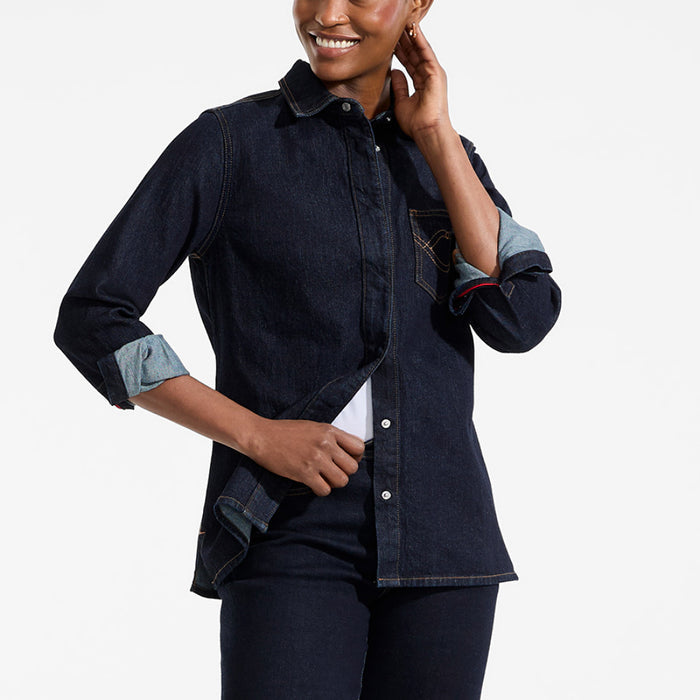 Woman wearing a dark denim shirt with rolled-up sleeves on a light gray background