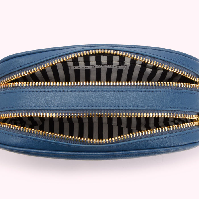 Overhead view of a blue Lulu Guinness crossbody bag open, showing the black and white striped interior and gold zippers.