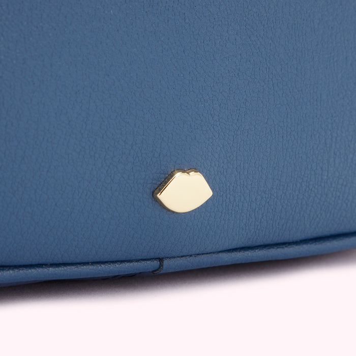 Close-up of a blue leather bag with a gold lip-shaped emblem.