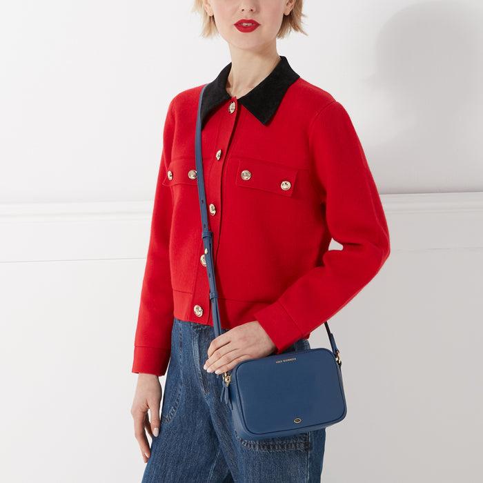 Woman in red cardigan and blue jeans with navy blue crossbody bag.