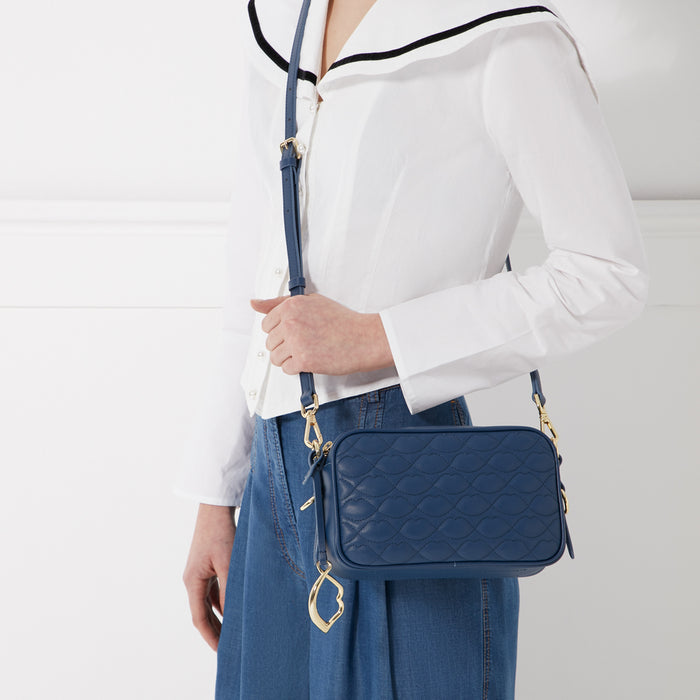 Woman wearing a white shirt and blue denim skirt carrying a quilted navy blue crossbody bag with gold accents.