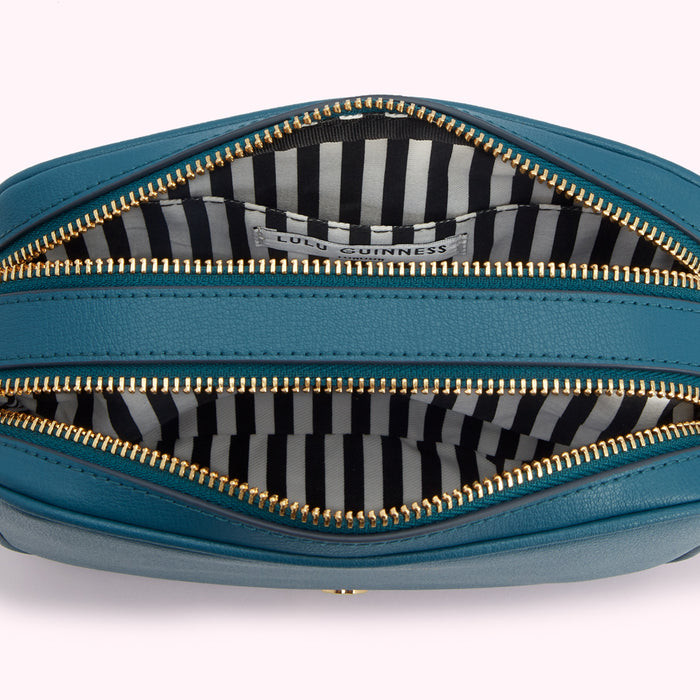 Interior of teal Lulu Guinness crossbody bag with gold zippers and black and white striped lining.