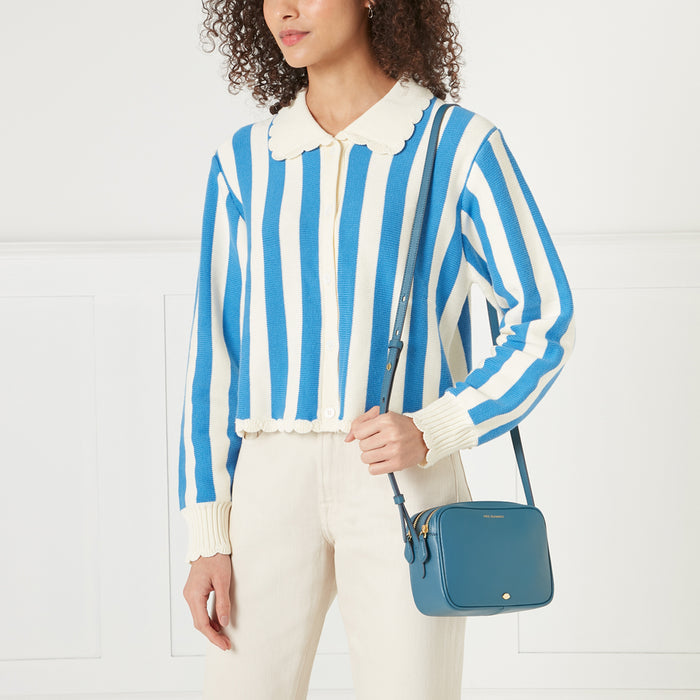 Woman wearing a blue and white striped cardigan and off-white pants holding a teal crossbody bag.