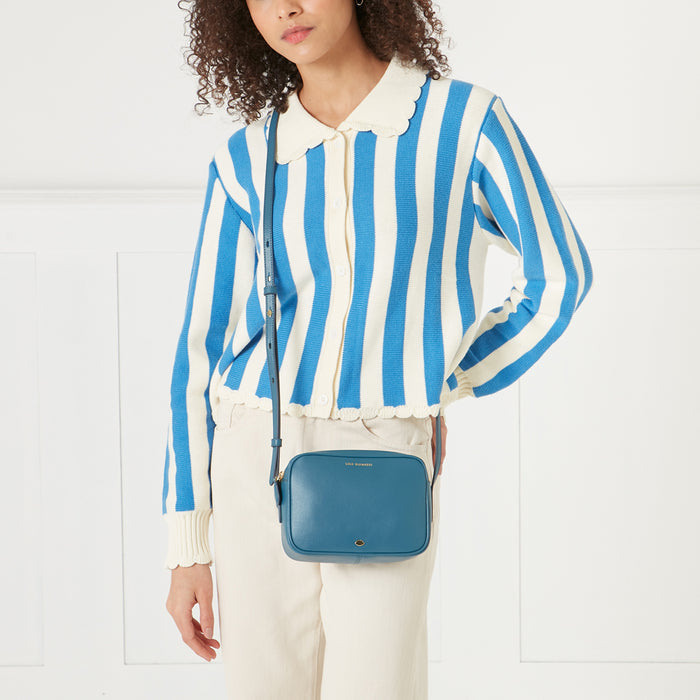 A woman in a blue and white striped cardigan carries a teal crossbody bag.