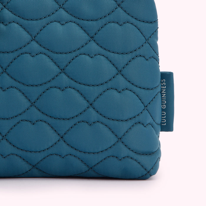 Close-up of a teal quilted Lulu Guinness makeup bag with a lip print pattern.