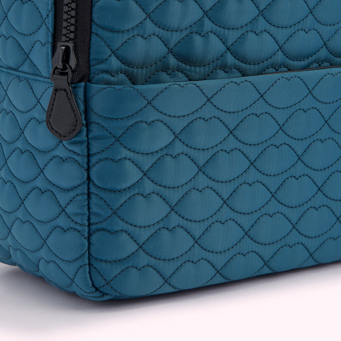Close-up of a teal quilted backpack with a black zipper and lip-shaped pattern.