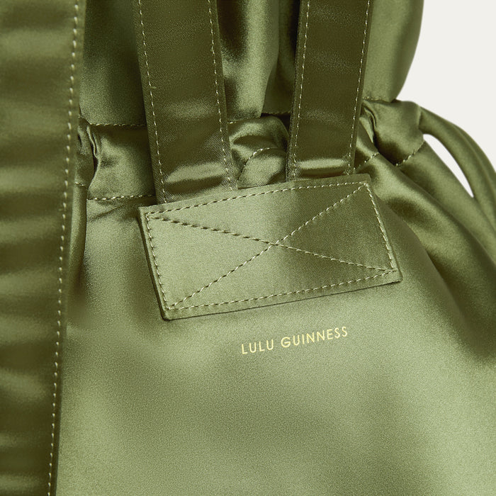 Close-up of a green satin backpack  with Lulu Guinness logo on a white background