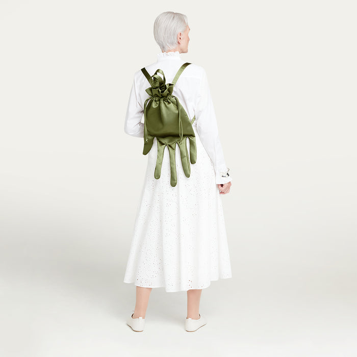 Person wearing a white shirt and white skirt with a green satin hand-shaped backpack on a plain background