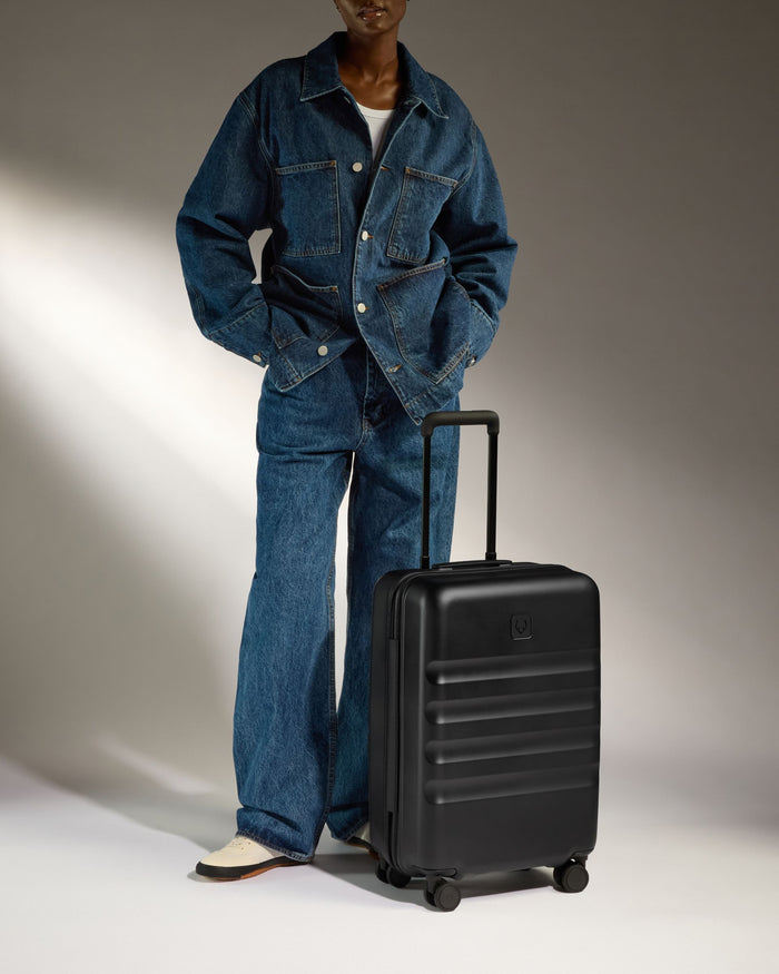 a man in a denim suit and hat standing next to a suitcase