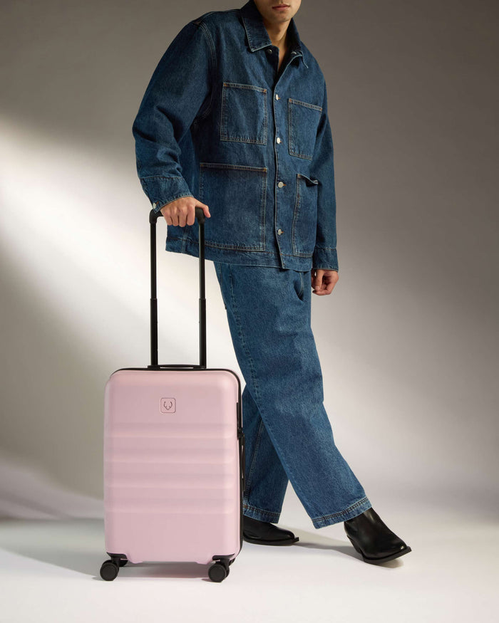 a man in a denim suit and jeans holding a pink suitcase