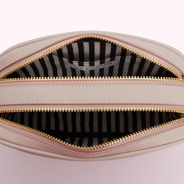 Interior of a pale pink Lulu Guinness crossbody bag with a black and white striped lining and gold zippers.