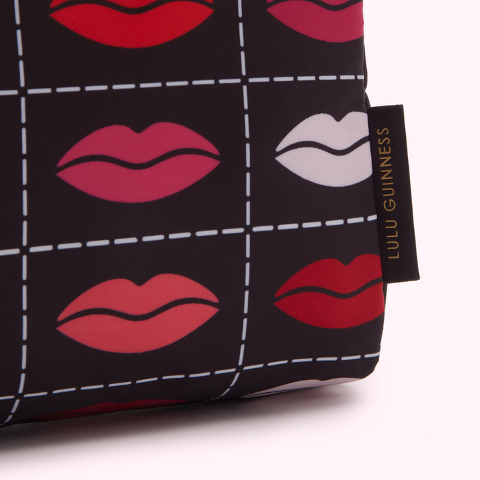 Close-up of a Lulu Guinness makeup bag with a black background and a repeated pattern of lips in various shades of red and pink.