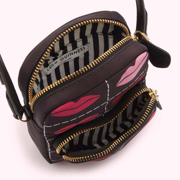 Black Lulu Guinness crossbody bag with red and pink lips print and gold zippers; the bag is open, showing a black and white striped interior.