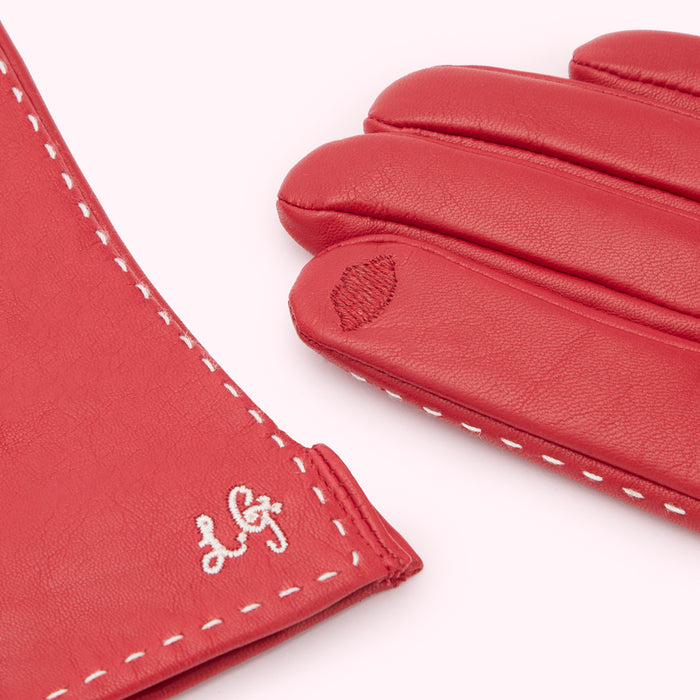 Close-up of a pair of red leather gloves with white stitching and a small embroidered logo.