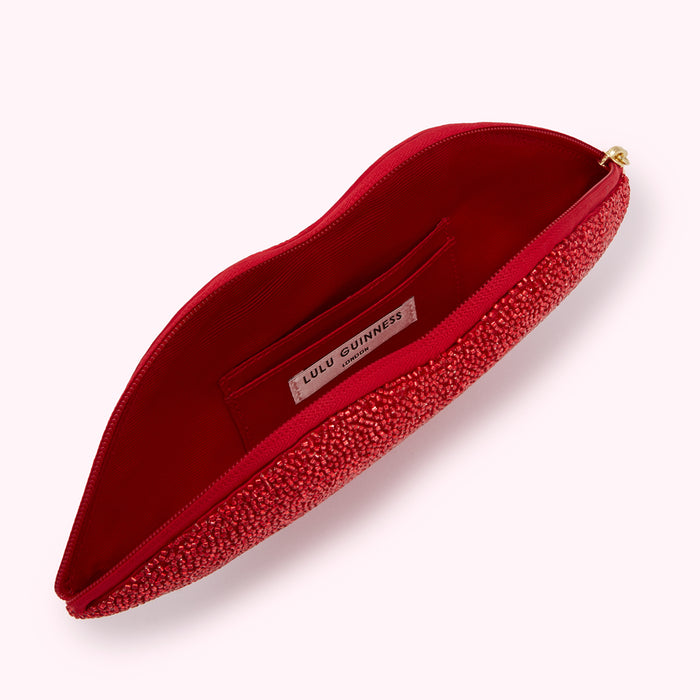 Red lip-shaped Lulu Guinness clutch open to reveal its red interior and brand label.