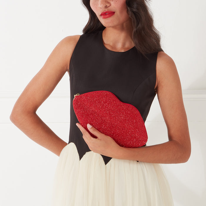Woman holding a red beaded lip-shaped clutch against a white background.