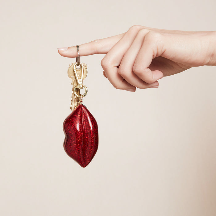 A glitter lip shaped keyring charm on a womens finger.