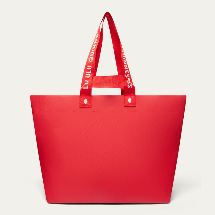 A red tote bag with wide shoulder straps printed with the white text 'LULU GUINNESS' shown on a light gray background.