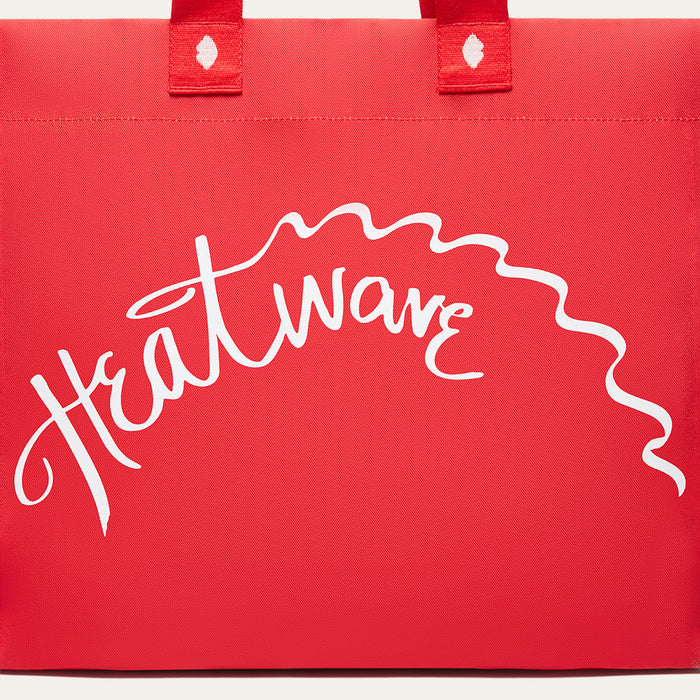 A red tote bag with white script text reading 'Heatwave' across the front and two red top handles, shown on a plain white background.