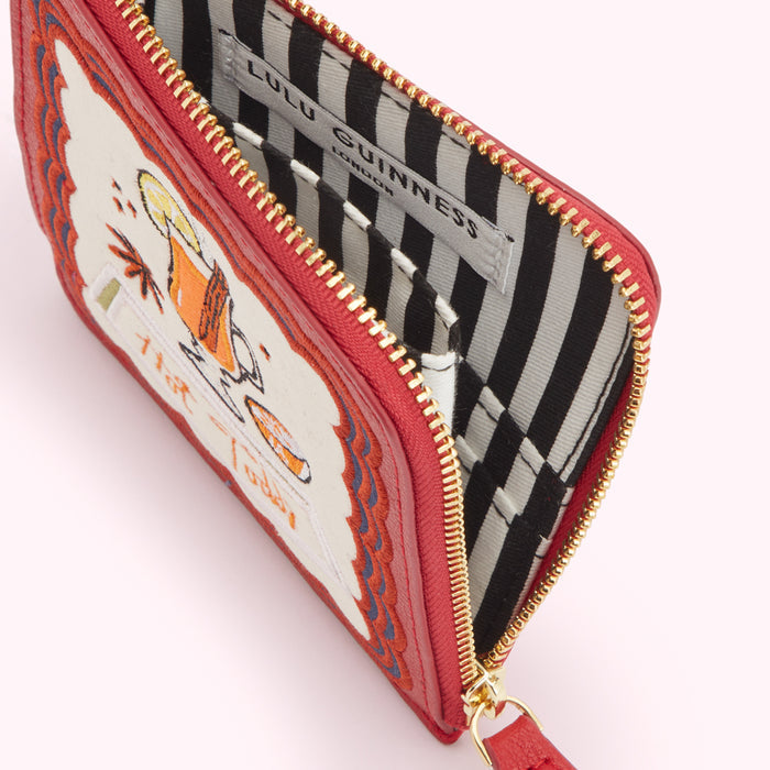 Red Lulu Guinness zip-around purse with an embroidered cocktail design and black and white striped interior.