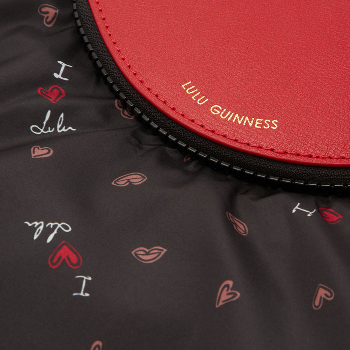Close-up of a red Lulu Guinness zipper pouch with a black background featuring a repeating pattern of lips and hearts.