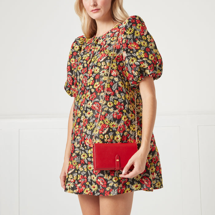 A woman in a floral dress holds a red crossbody wallet.
