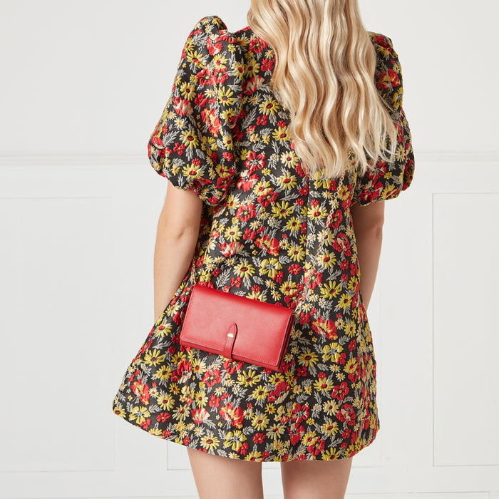 A woman wearing a black and floral dress with a red crossbody wallet.