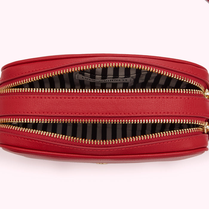 Red Lulu Guinness crossbody bag open to reveal black and white striped interior and gold zippers.