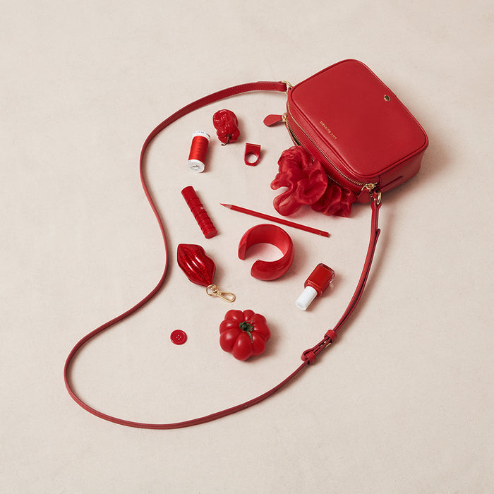Red handbag with matching accessories spilling out on a beige background