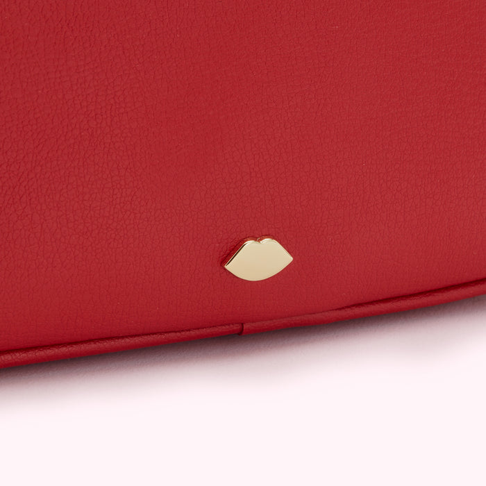 Close-up of a red textured leather purse with a gold lip-shaped logo.