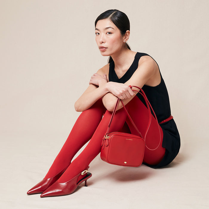 Woman sitting on the floor holding a red handbag against a beige background