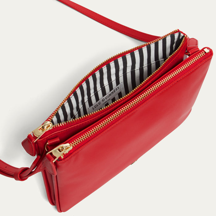 Red crossbody bag with gold zipper and black and white striped lining on a light gray background