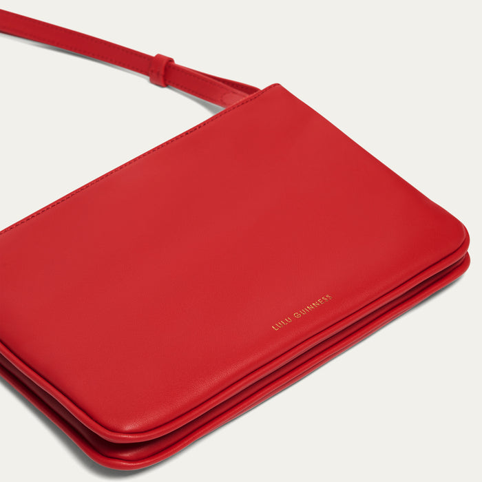 Red handbag with gold foil print 'Lulu Guinness' branding on a light gray background