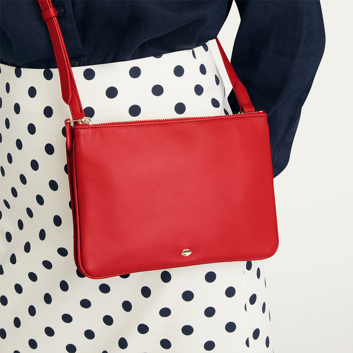 Red handbag held by a person wearing a polka dot dress on a plain background