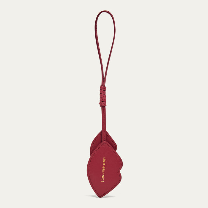 Back images of a red leather lip shaped charm with a foil printed 'Lulu Guinness' logo on a light grey background