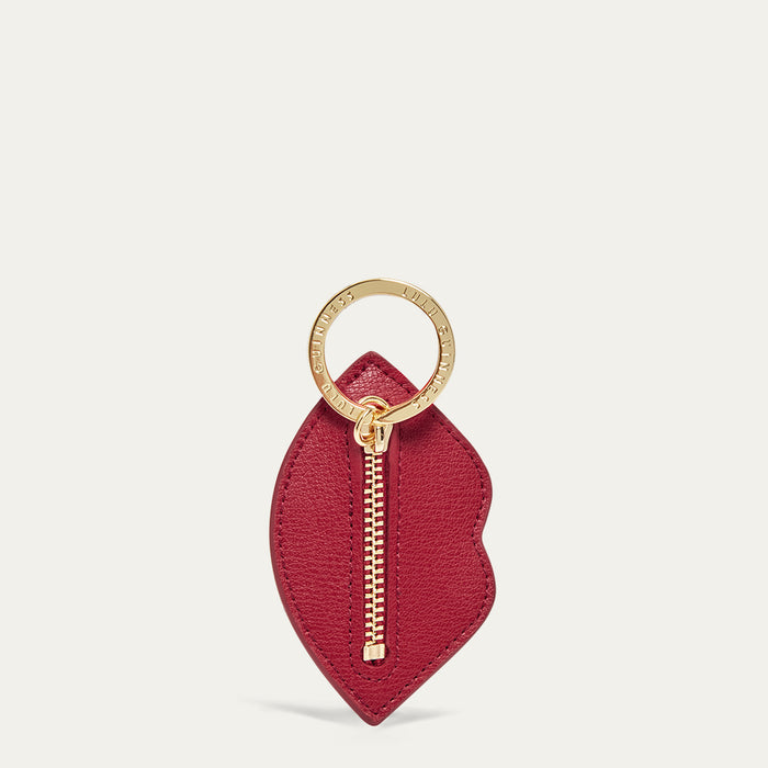 Red leather lip shaped keychain with gold zipper and ring on a light grey background