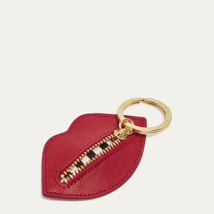 Red lip shaped keychain with gold zipper open to reveal a black and white striped lining on a light grey background