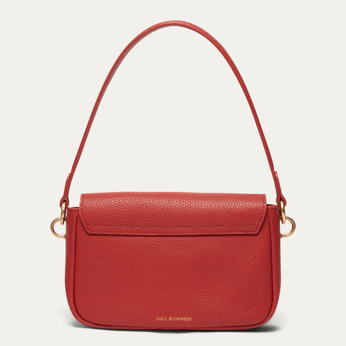 A red pebbled leather handbag with a flap front, gold-tone hardware, and a thin shoulder strap, shown against a light gray background. The brand name 'LULU GUINNESS' is printed in gold at the bottom center.