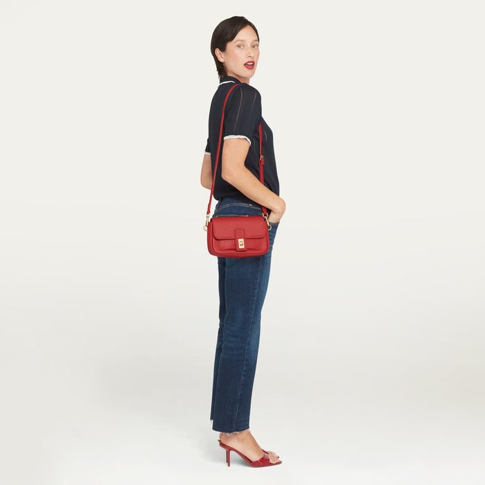 A women in a navy knit top, blue denim jeans and red shoes with a red leather crossbody bag.