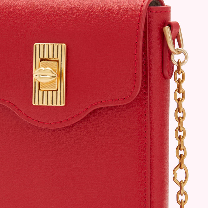 Close-up of a red leather handbag with a gold lip-shaped clasp and gold chain strap.