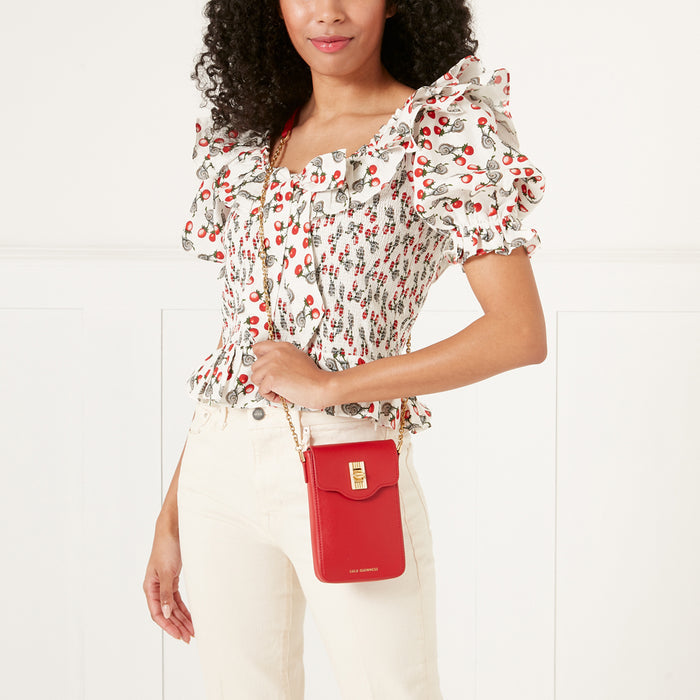 Woman in a white and red blouse and white pants holds a red Lulu Guinness crossbody bag.
